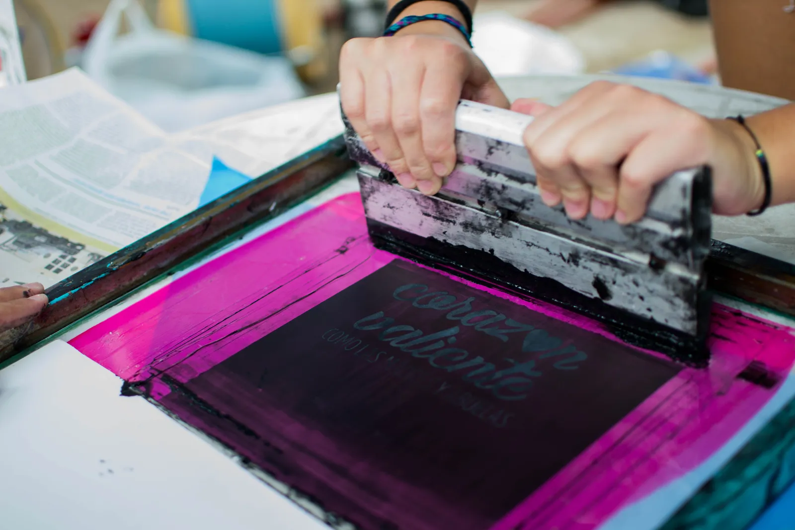 Printer pulling vivid pink ink across a screen on the press