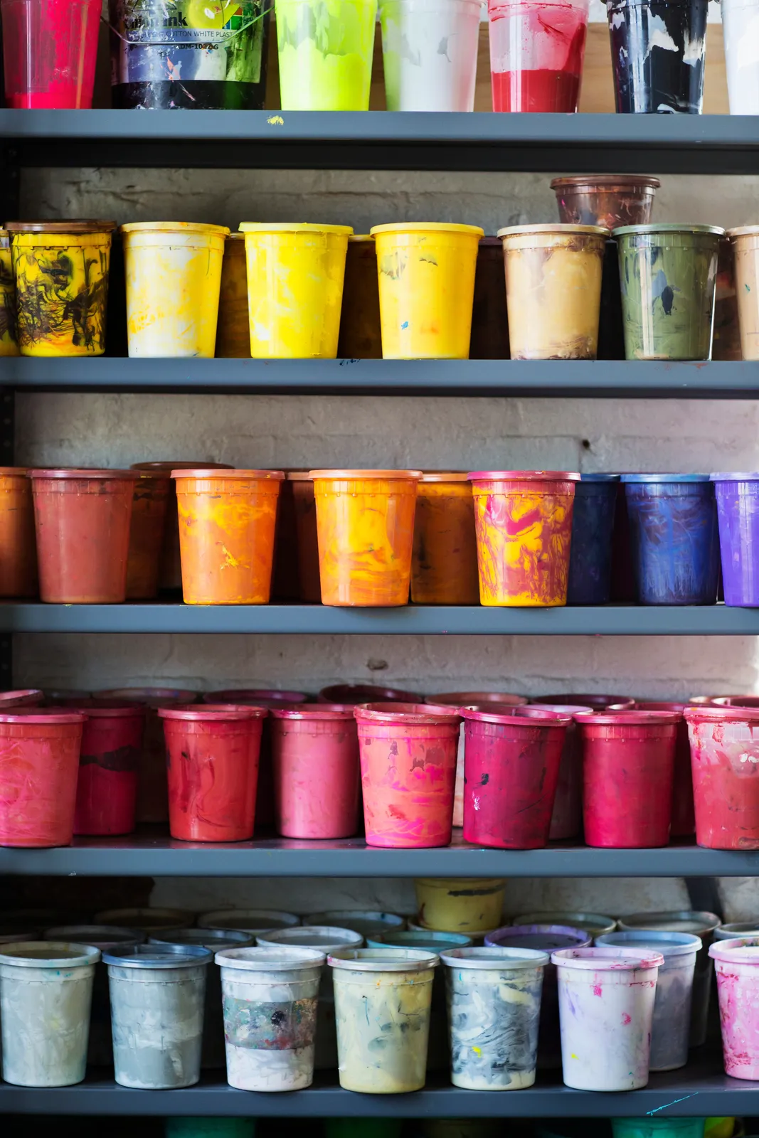 Shelves stacked with colorful buckets of plastisol ink in the print shop