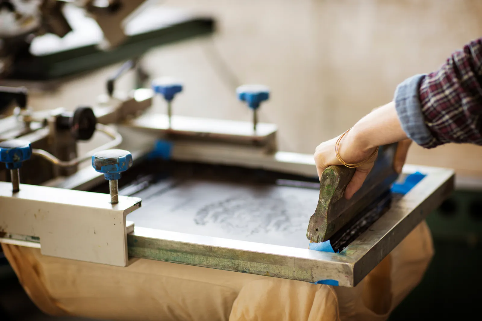 Printer pulling a squeegee across a screen on a manual press